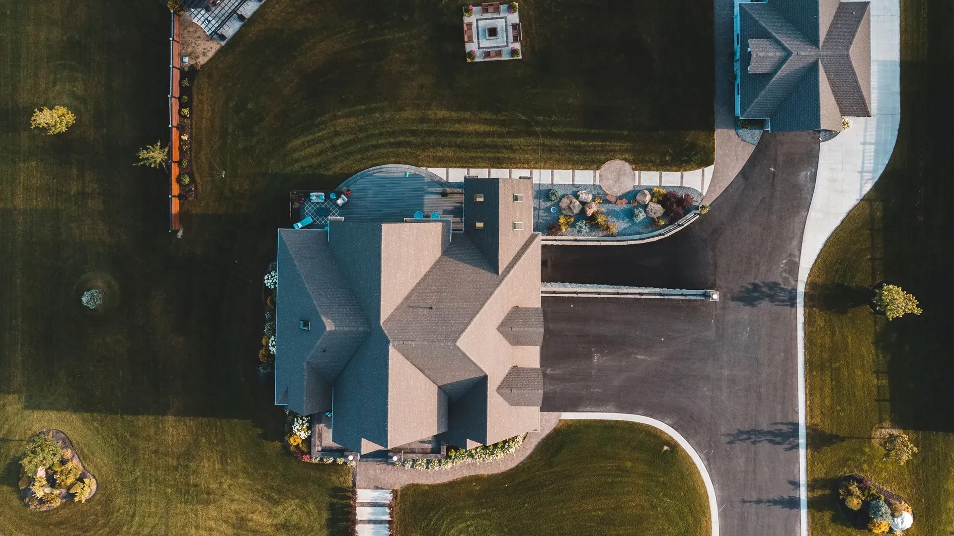 Overhead view of a single-family house on a landscaped lot, showing the roof, driveway, pool deck and a detached outbuilding